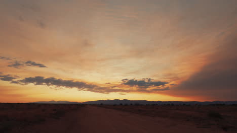 Looking-along-a-dirt-road-to-the-west-as-the-sun-sets-over-the-Mojave-Desert-landscape---static-time-lapse