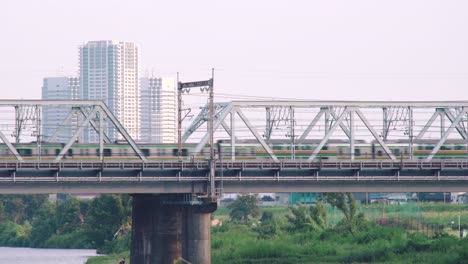 Tren-Jr-Cruzando-El-Puente-Ferroviario-Sobre-El-Río-Tamagawa-Con-Edificios-De-Gran-Altura-Al-Fondo-En-Tokio,-Japón