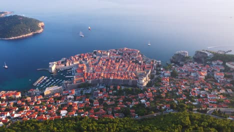 Stunning-reveal-view-flying-forward-into-sea-and-old-town-of-Dubrovnik,-Croatia-durning-sunset-with-mountains,-cable-car-and-sea-in-4k