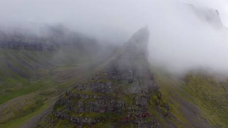 Imágenes-Vívidas-De-Nubes-Reunidas-Alrededor-Del-Pico-De-Montañas-Rocosas-Verdes-En-Una-Mañana-Brumosa-En-Islandia