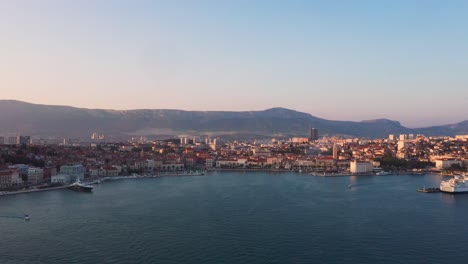 Aerial-view-flying-across-harbour-from-left-to-right-during-sunset-in-Split,-Croatia-with-mountains-and-sea-in-4k