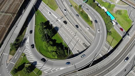 Round-circular-European-asphalt-highway-off-and-on-ramp,-cars-and-traffic-traveling-on-expressway-and-entering-and-exiting-on-sunny-day,-static-overhead