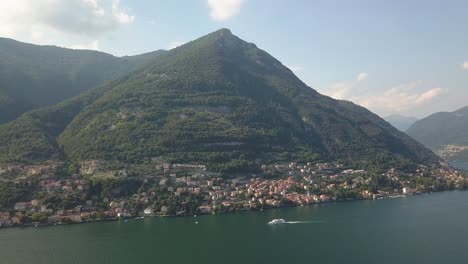 A-large-green-mountain-next-to-a-lake-with-a-big-boat-driving-by-in-Italy,-Como-lake