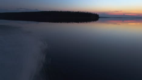 Camera-pan,-starting-from-the-side-of-a-speeding-boat-at-water-level-to-the-beautiful-colourful-sunset-on-a-lake