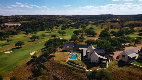 Mansion-on-hill-overlooking-golf-course-aerial-fly-ver-orbit-with-people-in-swimming-pool-on-sunny-day-with-blue-sky-at-Texas-country-club