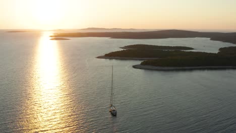 Sonnenreflexion-Auf-Einem-Ruhigen-Meer-Mit-Hohem-Segelboot-Neben-Waldinseln