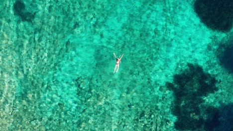 Aerial-tracking-shot-of-a-woman-swimming-off-the-coast-of-Losinj-island,-Croatia-from-high-above