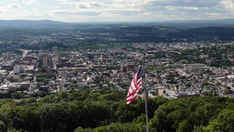 American-flag-flies-proudly-on-mountain-overlooking-American-city-on-summer-day,-Reading-Pennsylvania-USA,-United-States-pride,-patriotic-theme-in-urban-city