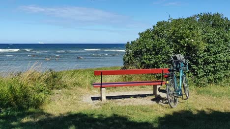 Static-shot-of-bike,-park-bench-and-green-bush-by-ocean-on-windy-day