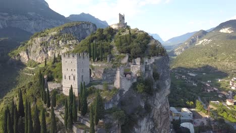 Zoom-out-drone-shot-in-4k-of-an-old-castle-fortress-on-top-of-a-hill-mountain-cliff-side,-Arco,-Riva-del-garda,-Trentino