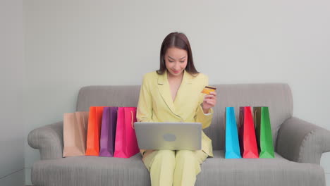 Frau-Nutzt-Laptop-Computer-Für-Online-Einkäufe,-Viele-Einkaufstaschen-Auf-Dem-Sofa