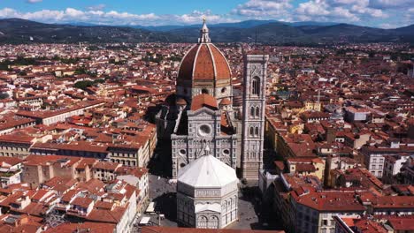 Aerial-view-of-Cathedral-of-Santa-Maria-del-Fiore-flying-and-zooming-in-with-city-and-mounatins-on-a-sunny-day-in-Florence-in-Italy-in-4k
