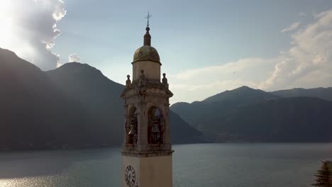 Church-clock-tower-at-the-beautiful-Como-lake-and-mountains-in-the-background-with-sunshine-in-Nesso,-Italy