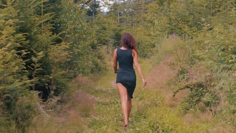 Rücken-Einer-Sexy-Frau-In-Einem-Schwarzen-Kleid,-Die-Barfuß-Auf-Grünem-Gras-In-Der-Waldnatur-Läuft