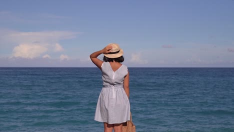 Back-of-girl-in-summer-dress-standing-in-front-of-wide-open-Ocean-Horizon-on-bright-and-sunny-day-SLOW-MOTION