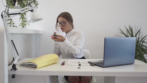 A-woman-primps-and-fixes-her-make-up-at-her-desk-while-at-work-in-a-clean-modern-office