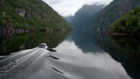 Aerial-shot-of-a-motorboat-gliding-on-a-fjord-in-Norway-amongst-mountains-with-green-trees