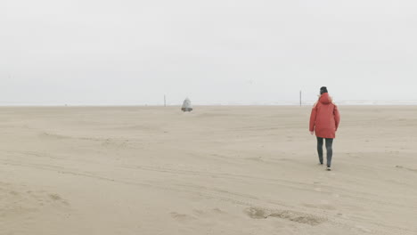 Rückansicht-Eines-Mädchens-Mit-Roter-Jacke,-Das-An-Einem-Kalten-Morgen-In-Den-Niederlanden-Am-Sandstrand-Von-Ijmuiden-Spazieren-Geht
