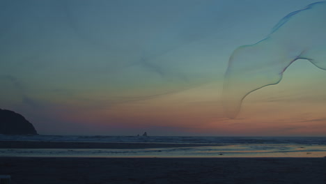 Giant-bubble-floats-across-vivid-sunset-beachscape,-blue-hour