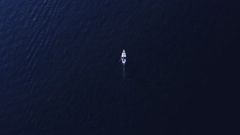Aerial-top-view-of-small-boat-slowly-moving-in-deep-dark-purply-blue-sea