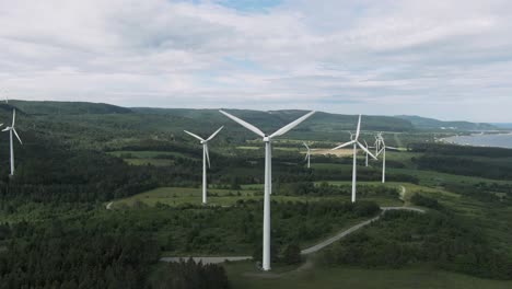 Luftaufnahme-Von-Windkraftanlagen-Auf-Dem-Riesigen-Feld-Mit-Grünen-Bäumen-An-Der-Küste-Des-Golfs-Von-Saint-Lawrence-In-Quebec,-Kanada-–-Schwenk-Drohnenaufnahme