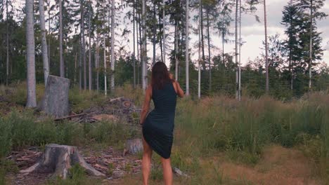 Rear-view-of-young-carefree-girl-wearing-dark-blue-dress-dances-in-nature,-slow-motion,-circle-pan,-sunset