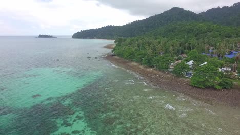 aerial-tracking-shot-of-tropical-island-coastline-with-ocean,-islands-and-pans-around-to-reveal-small-Thai-style-resorts-and-telecommunication-towers