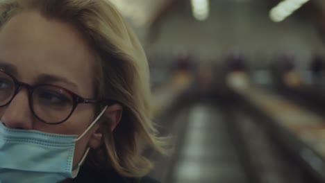 Girl-With-Eye-Glasses-And-Disposable-Face-Mask-Riding-Escalator-Moving-INside-The-Building-During-The-Pandemic-Coronavirus