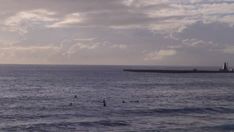 Silhouette-view-of-group-of-surfers-waiting-for-waves-in-ocean-on-bright-and-sunny,-cloudy-day---long-shot