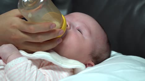 Neugeborenes-Mädchen-Trinkt-Säuglingsnahrung-Aus-Der-Flasche-Zu-Hause,-Nahaufnahme,-Hände,-Plastikflasche-Und-Kopf-Des-Babys