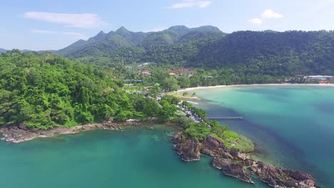 Tropical-Koh-Chang-island-dense-mountain-woodland-idyllic-turquoise-bay-coastline-aerial-view-descending