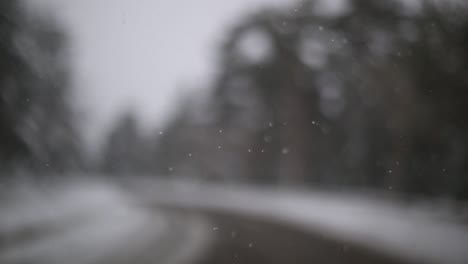 Slow-motion-snowy-falling-into-the-car,-unfocus-road-at-the-background,-road-trip-Spain