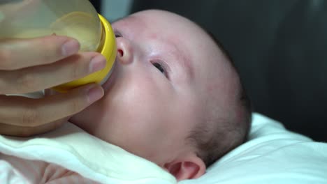 Neugeborenes-Mädchen-Saugt-Milchnahrung-Aus-Der-Kleinkindflasche,-Nahaufnahme-Auf-Gesicht-Und-Mutters-Hand