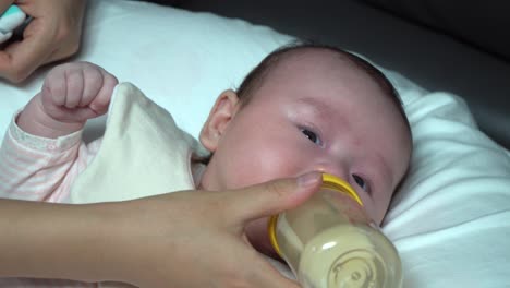 Newborn-infant-baby-curiously-looking-into-the-camera-while-drinking-formula-milk-from-the-bottle-close-up