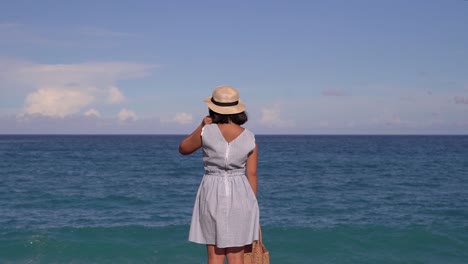 Back-of-girl-in-summer-dress-standing-in-front-of-wide-open-Ocean-Horizon-on-bright-and-sunny-day