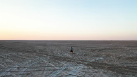 Aerial-View-of-Male-Figure-Walking-on-Massive-Salt-Flats-Field-Under-Sunset-Sun