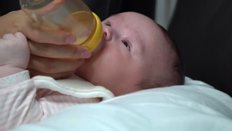 Newborn-infant-baby-girl-drinking-formula-milk-from-the-bottle-close-up-slide-in-side-angle