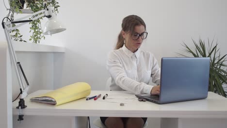 An-attractive-woman-at-her-desk-in-the-office-types-on-her-laptop-in-a-clean-modern-workplace