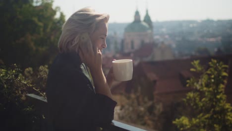 Geschäftsfrau-Auf-Dem-Balkon-Lacht-Beim-Telefonieren-Und-Trinkt-Eine-Tasse-Heißen-Kaffee