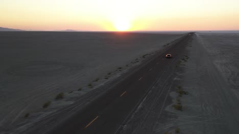 Aerial-View-of-Car-Moving-on-Straight-Desert-Road-With-Sunrise-Sun-Above-Valley