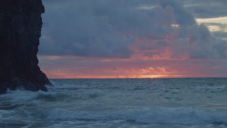 Wolken-Leuchten-Mit-Atemberaubendem-Sonnenuntergang,-Wenn-Wellen-In-Der-Nähe-Der-Küstenklippen-Zusammenbrechen