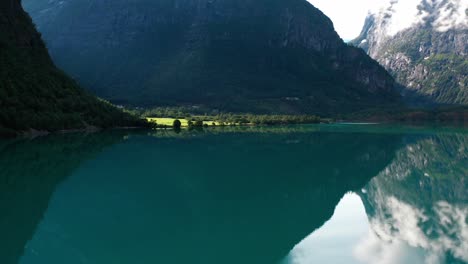 Calm-Waters-Of-Blue-Lake-With-Green-Field-And-Mountains-In-Norway