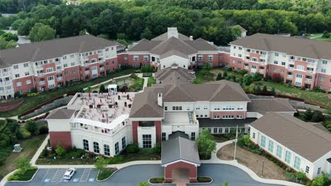 Aerial-pullback,-apartments-at-senior-living-retirement-home-complex,-multistory-residential-buildings-and-meeting-space,-American-flag,-United-States-of-America,-retirement-and-senior-citizen-aging