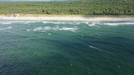 AERIAL:-Pan-Tracking-Shot-of-Surfers-Near-the-Sandy-Beach-on-a-Bright-Day