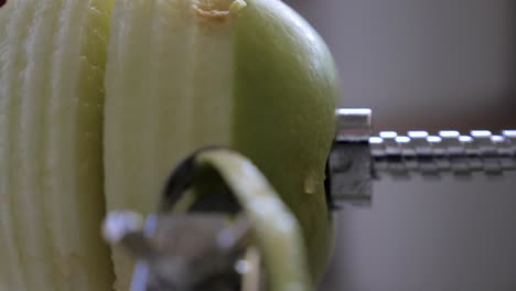 Slow-motion-of-person-struggling-to-finish-peeling,-cutting-and-core-green-juicy-apple-skin-with-metal-device-in-kitchen-with-water-droplet