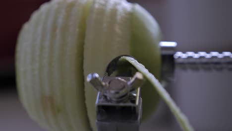 Slow-motion-metal-kitchen-device-peeling,-cutting-and-core-green-juicy-apple-skin-and-flesh-on-kitchen-bench-with-juice-flying-out