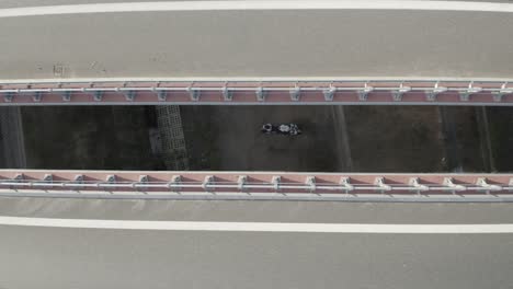 Aerial-drone-view-of-a-motorcycle-parked-under-a-bridge-through-the-gap-between-two-bridges-on-a-highway