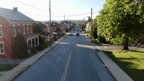 Aerial-drone-flight-above-traffic,-cars,-trucks-pass-by-traditional-old-homes-along-street,-sidewalk,-summer-magic-hour-in-United-States-of-America,-USA