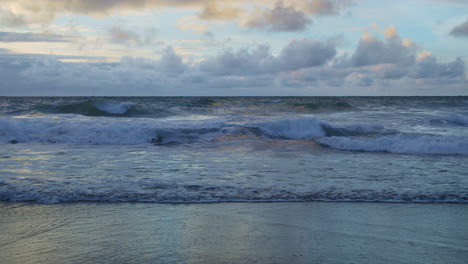 Colorful-morning-clouds-over-rolling-beach-waves,-slow-motion