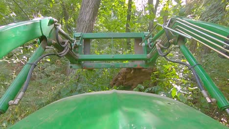 POV-of-equipment-operator-using-a-loader-with-forks-to-move-a-dug-up-tree-stump-on-a-sunny-day-in-the-woods